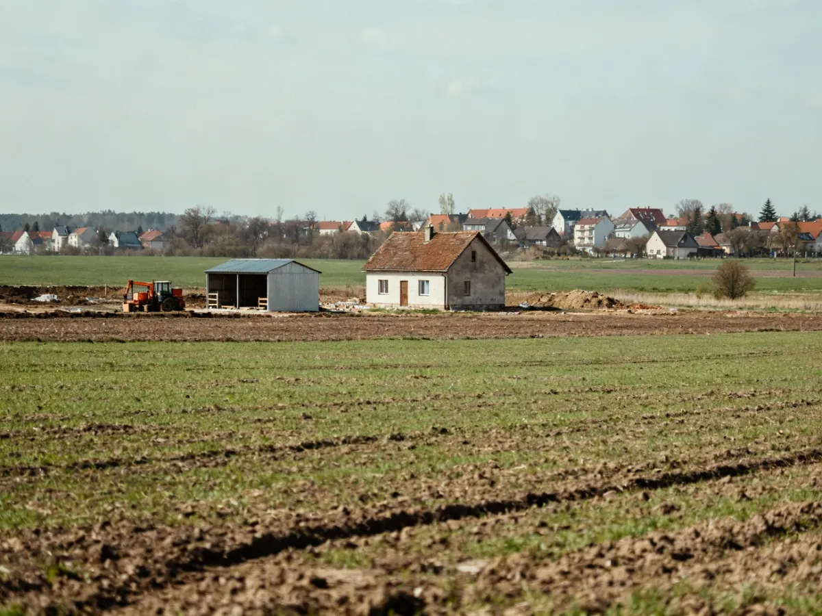 Działka rolna z polami i zabudową wiejską w tle